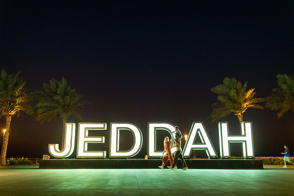 Une famille se promène devant les lettres géantes « Jeddah » au bord de la plage.